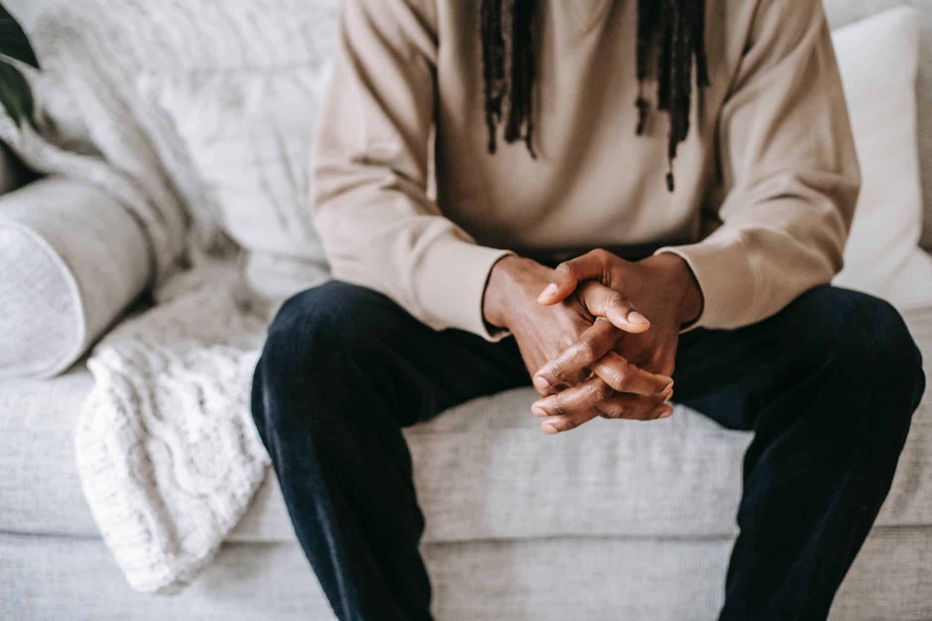 crop thoughtful black man with clasped hands on sofa